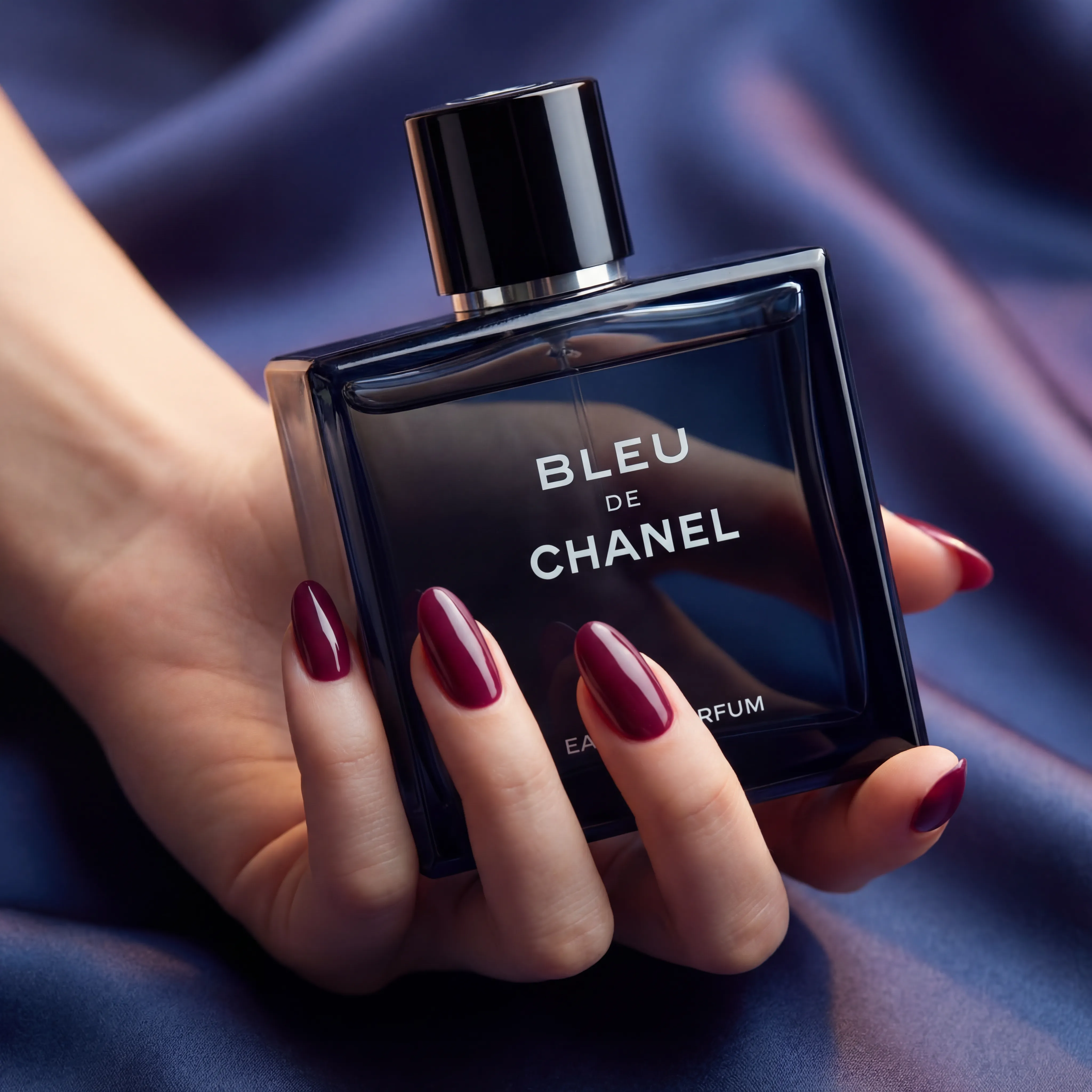 Blue perfume bottle held in hand against deep blue silk